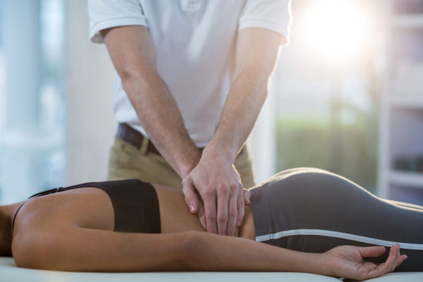 Male physiotherapist giving back massage to female patient in clinic
