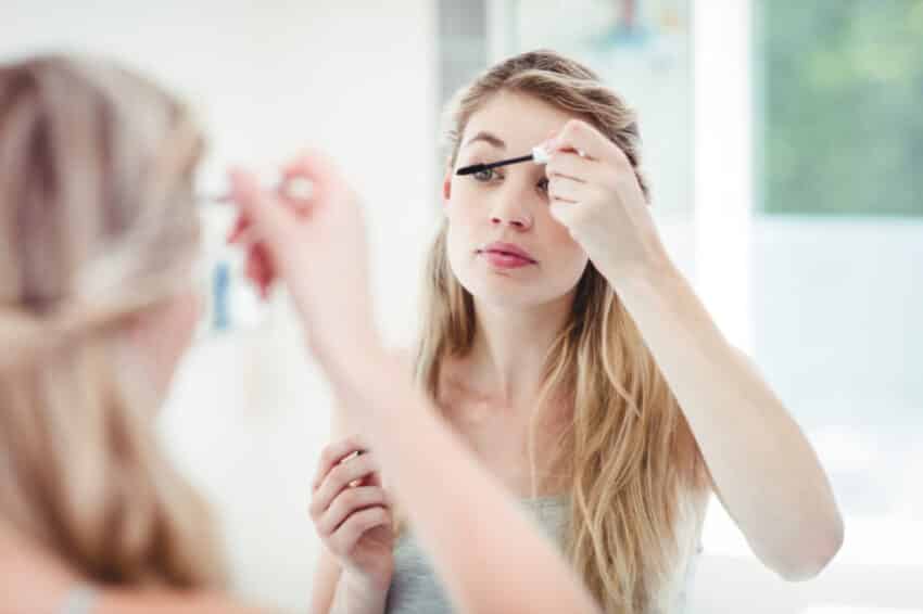 Young woman applying mascara while looking in mirror