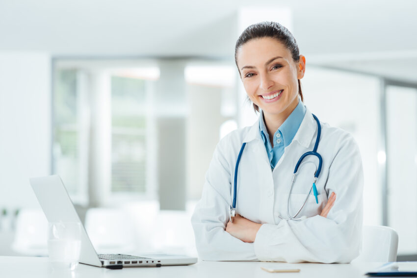 Confident,Female,Doctor,Sitting,At,Office,Desk,And,Smiling,At