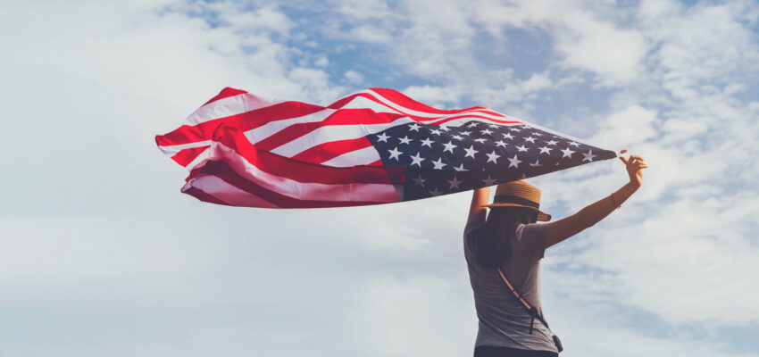 Young,Woman,Holding,American,Flag,On,Blue,Sky,Background,With
