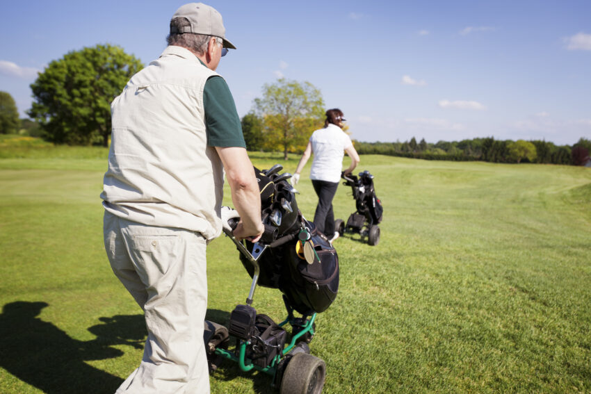 Active,Senior,Golf,Couple,Pushing,Golf,Trolley,With,Bag,On